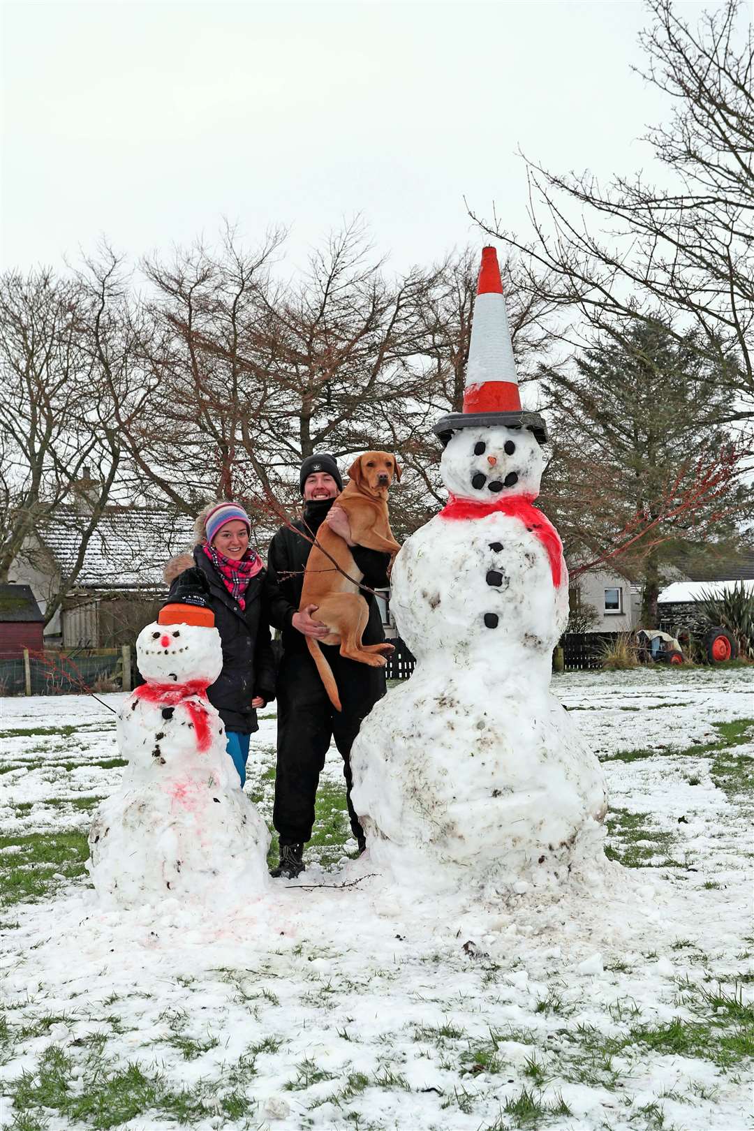 Terri Munro and Jamie Morris pose beside their snowmen creations in Halkirk along with their dog Rodney. Picture: James Gunn