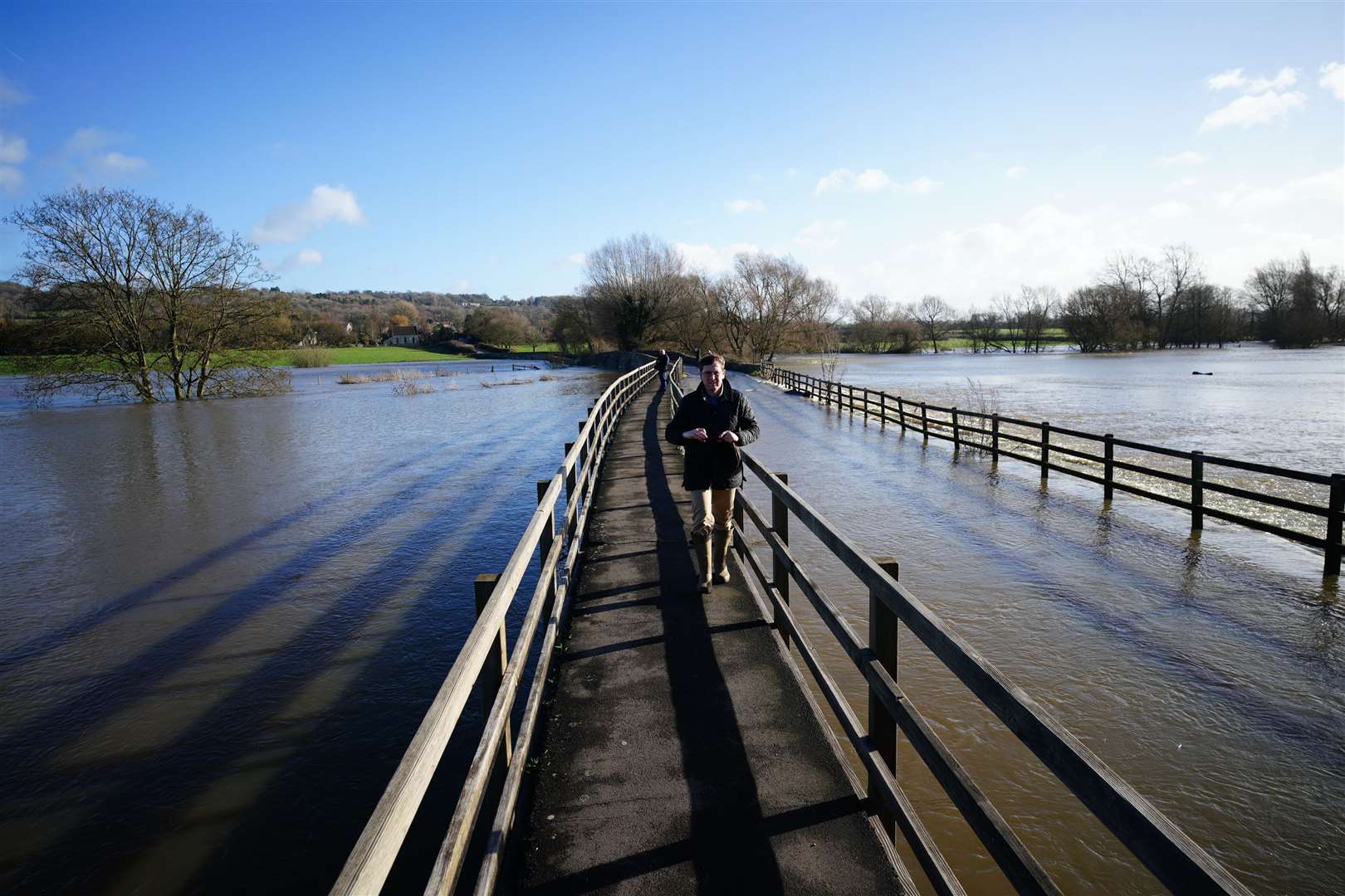 People walk across a raised footpath on a bridge flooded by the River Avon, in Lacock, Wiltshire (Ben Birchall/PA)