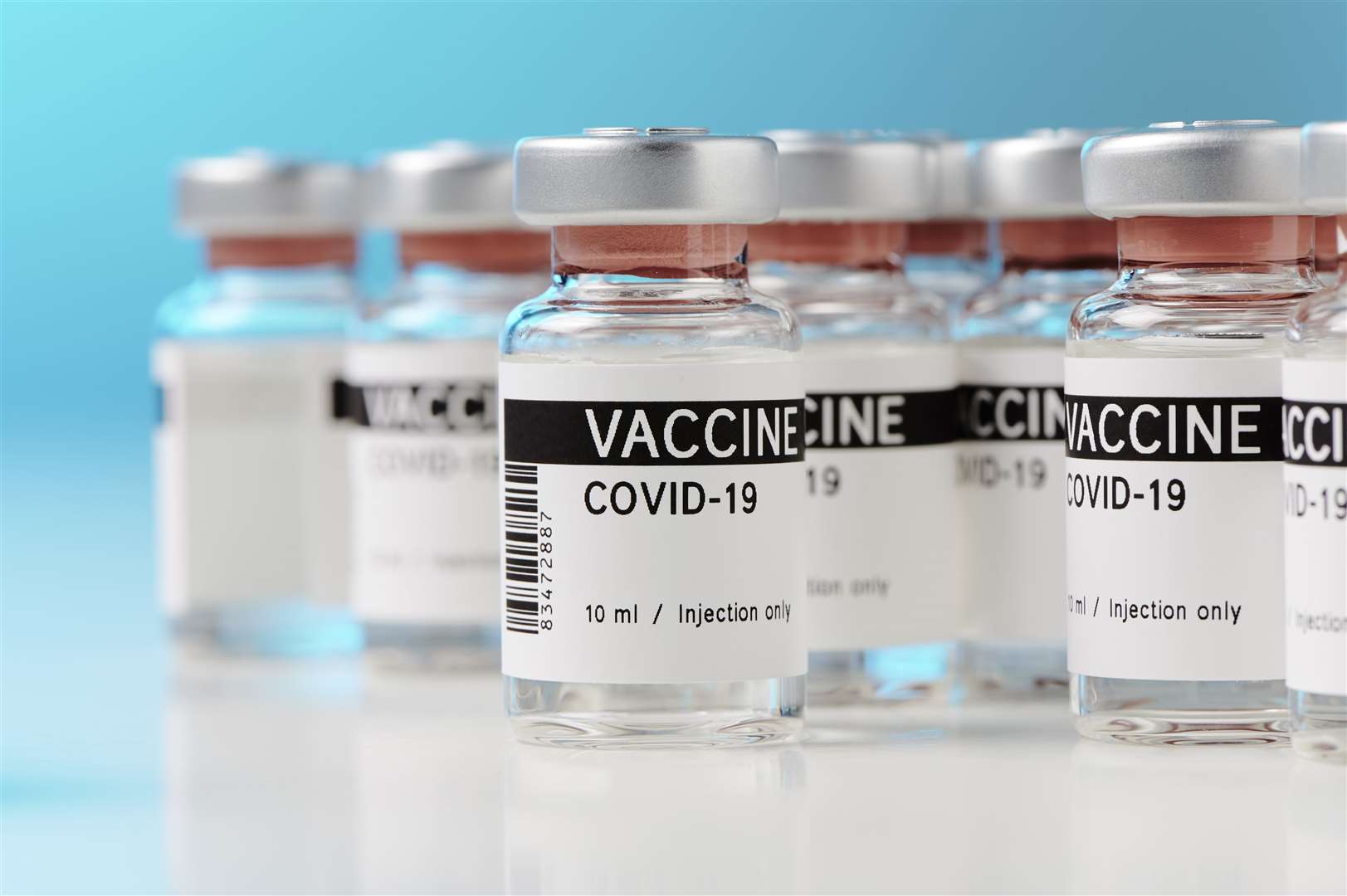 Some ampoules with clear liquid. The vials contain Covid-19 vaccine. The vials are placed in a laboratory against a blue background