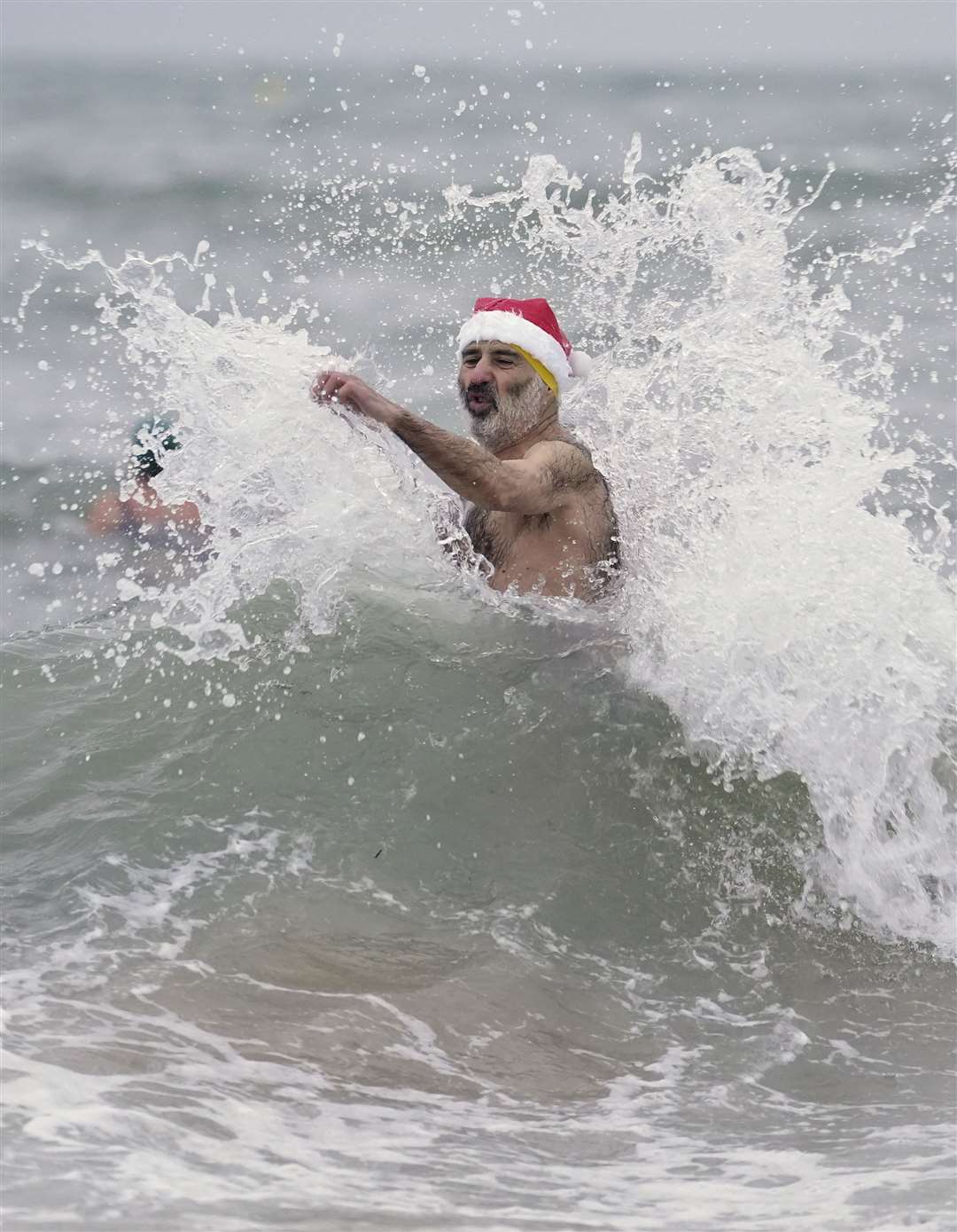 A man in a Santa hat braves the waves during his bracing swim (Andrew Matthews/PA)