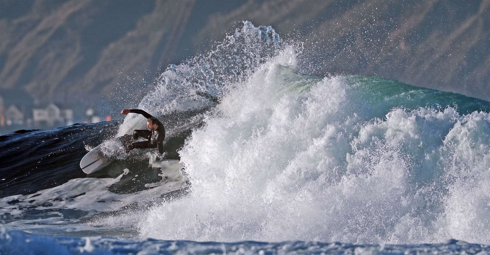 A surfer swoops down from the crest of a wave at full speed.