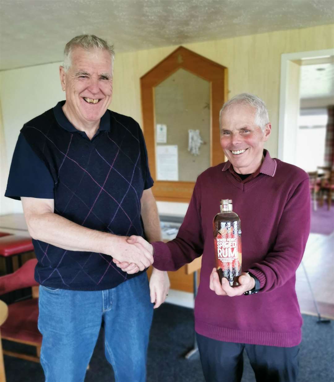 Alex Anderson (left) receiving a bottle of North Point spiced rum from Sandy Chisholm after winning the nearest-the-pin prize during the latest round of the Senior Stableford competition at Reay.