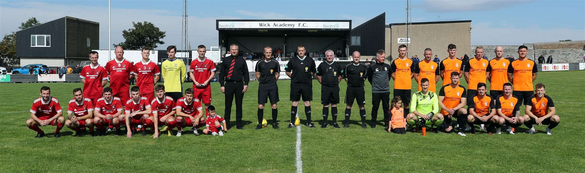 Wick Groats and Avoch players and managers, along with the two mascots and four match officials, line up prior to kick-off at Harmsworth Park. Picture: James Gunn