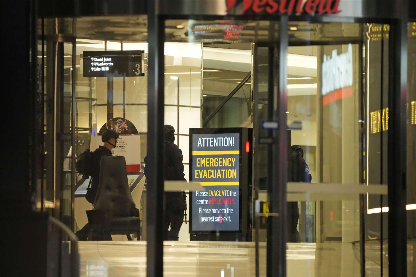 Police officers walk past a sign to evacuate at the shopping centre (Rick Rycroft/AP)