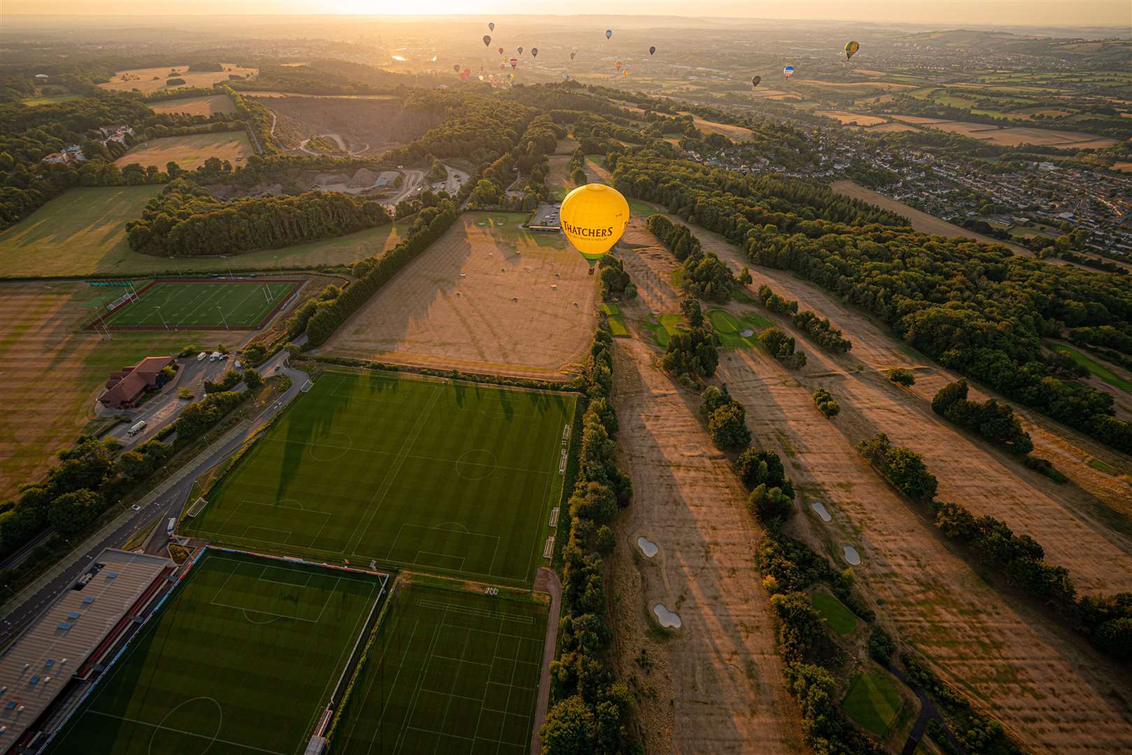 A hot air balloon flies over a browning and parched golf course (Ben Birchall/PA)