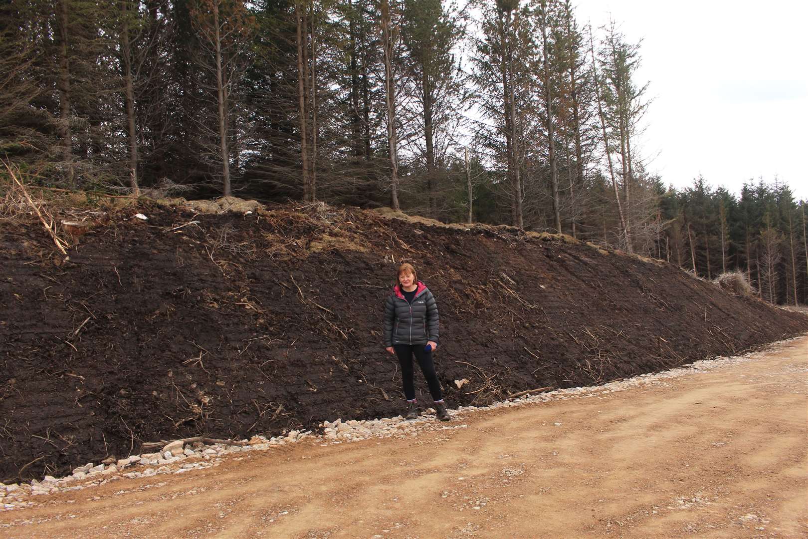 Jillian Bundy standing against a high embankment of exposed peaty ground beside the Limekiln access road.