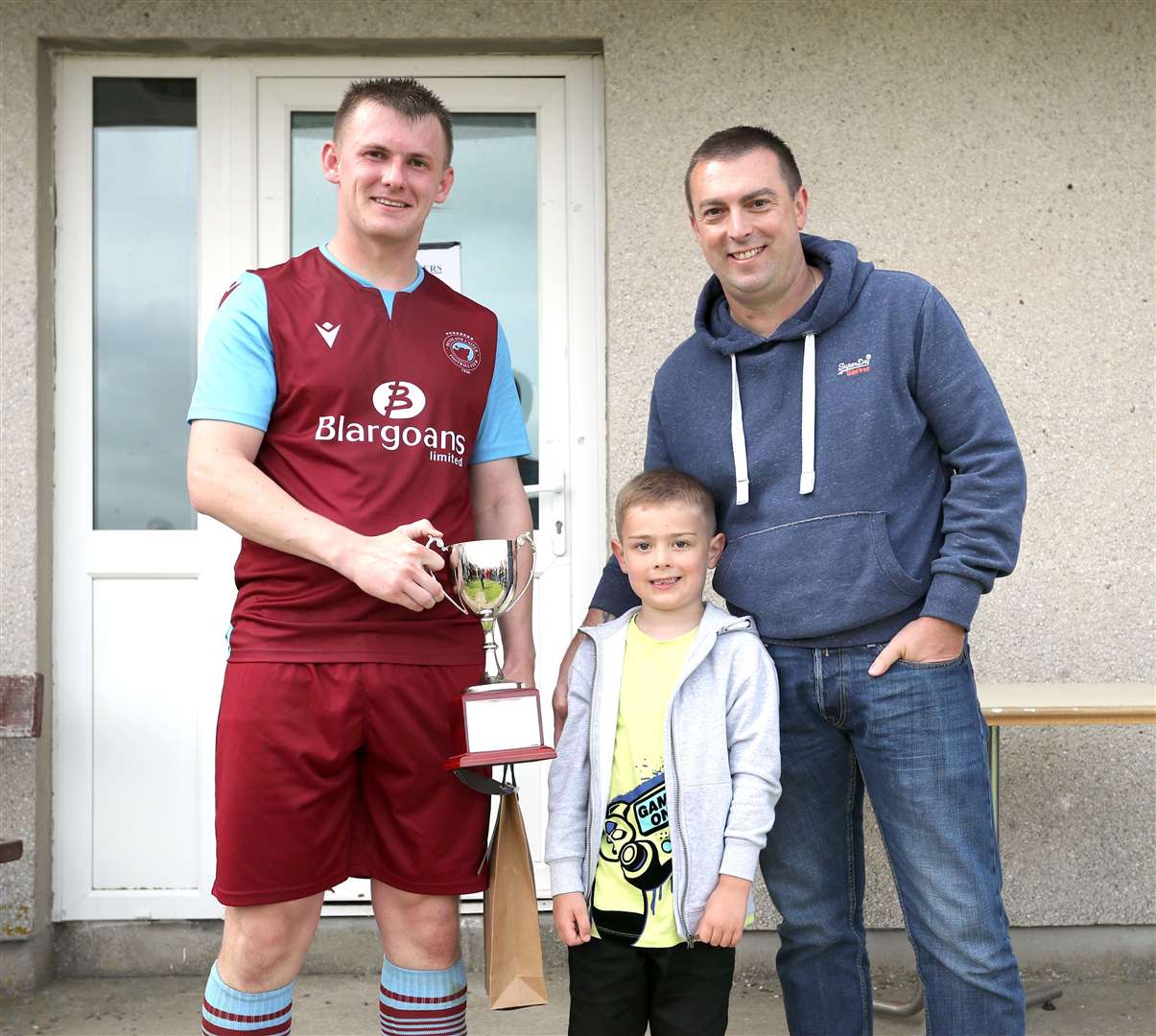 Andy Mackay accepts the man of the match trophy – the Alan (Bobo) Mackay memorial cup – from the late Alan's son David and his grandson Finn. Picture: James Gunn