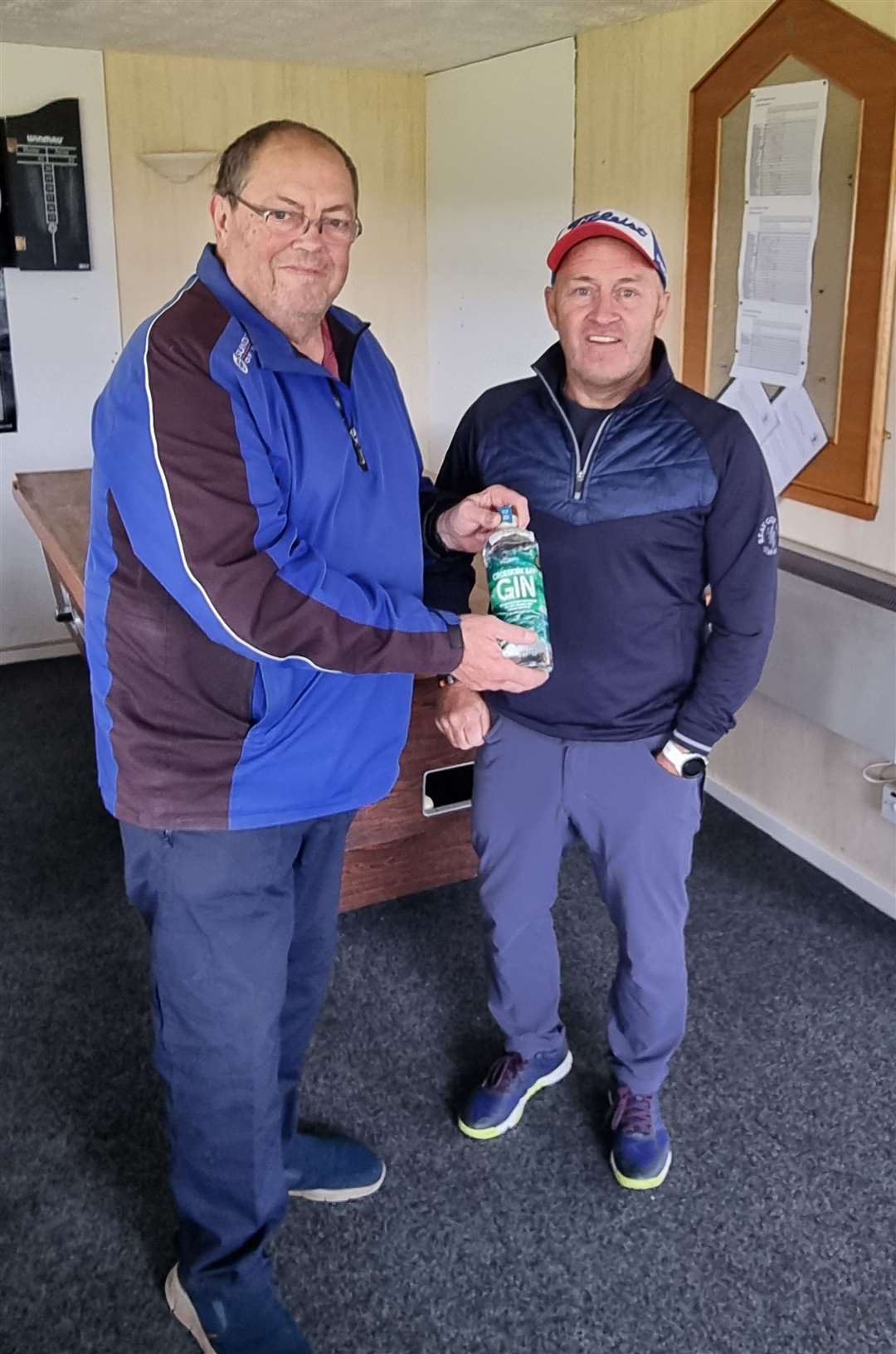 Willie Steven (right) receives a bottle of North Point gin after winning the nearest-the-pin prize in round two of the Senior Stableford competition.