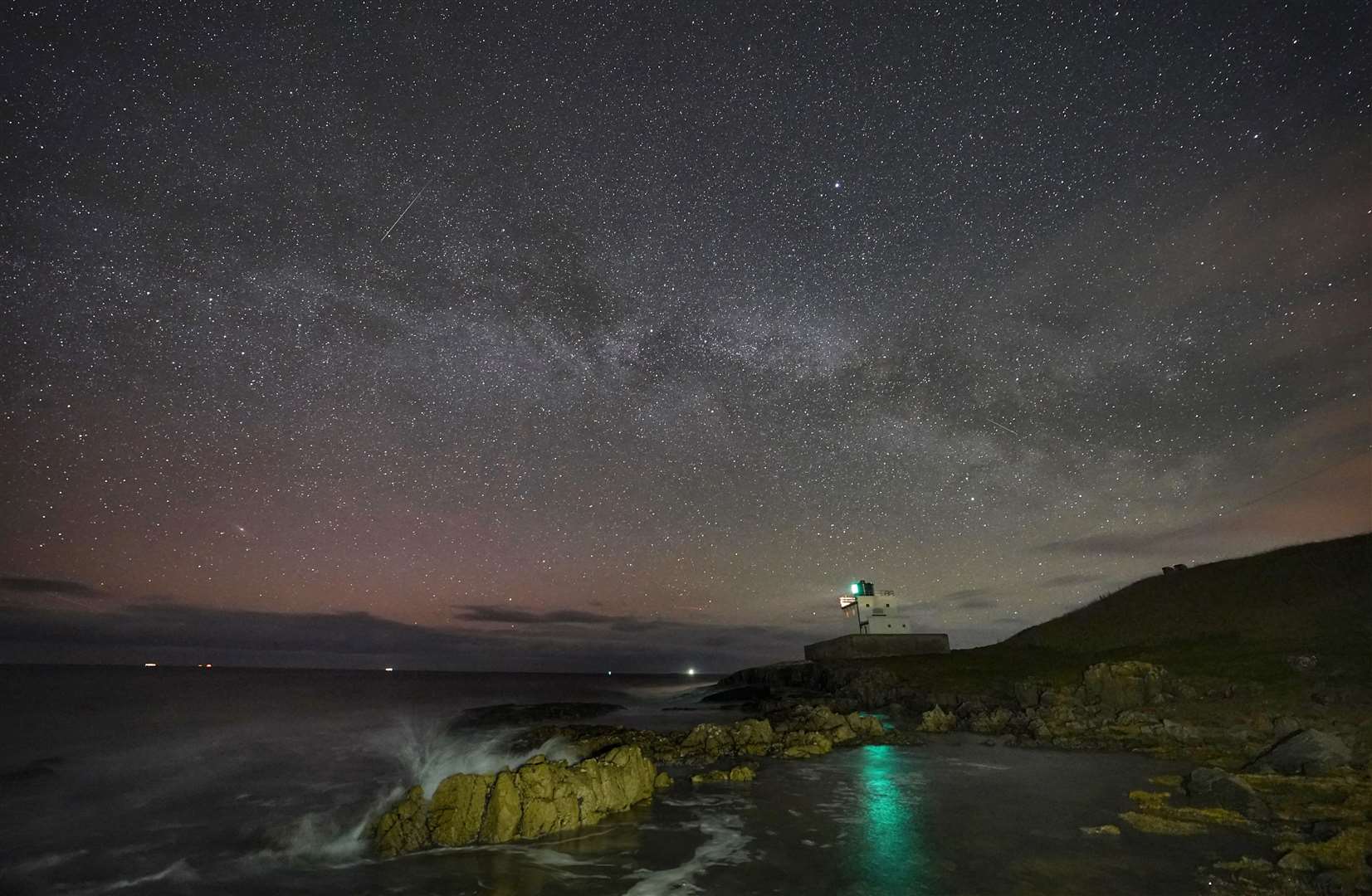 The Milky Way core rises over Bamburgh Lighthouse in Northumberland (Owen Humphreys/PA)