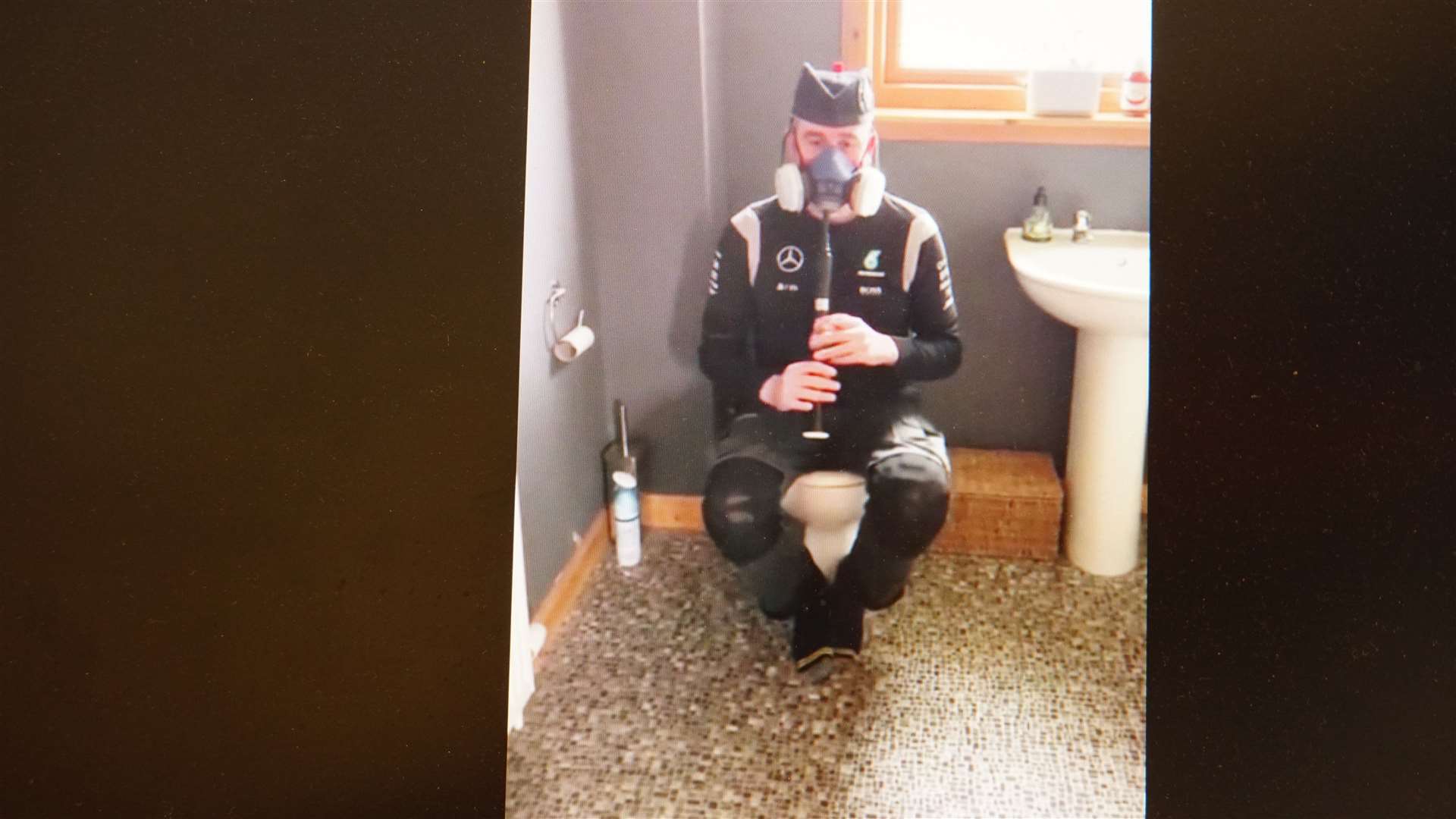 A frame grab from the hilarious video shows piper Alan Plowman, who has played in the band since 1988, sitting on the toilet and wearing a protective mask.