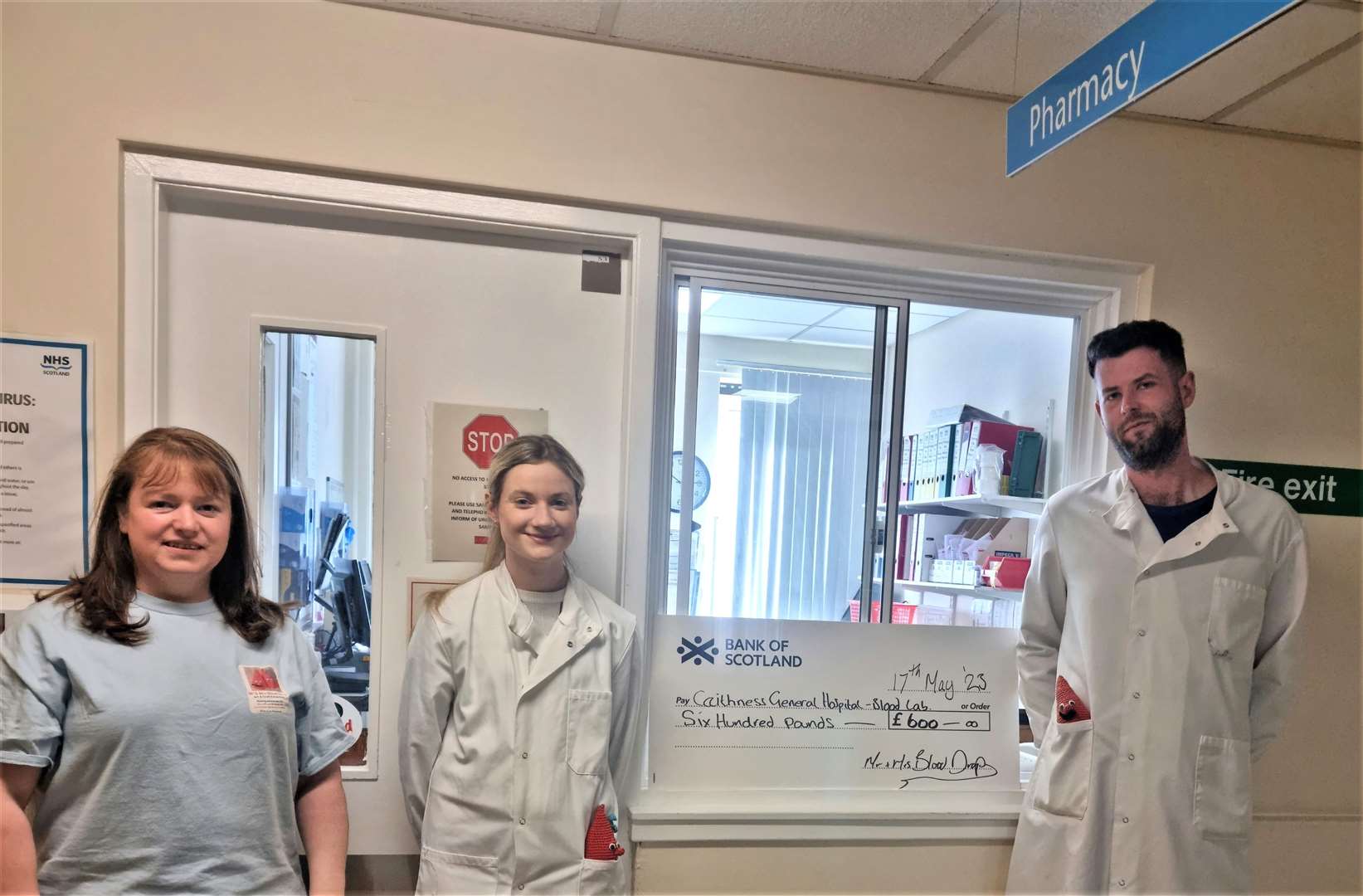 Joy Jackson, at left, hands over the £600 cheque to lab workers at the Wick hospital Chloe MacDonald and Ryan Shearer who have Mr and Mrs Blood Drop gonks in their pockets.
