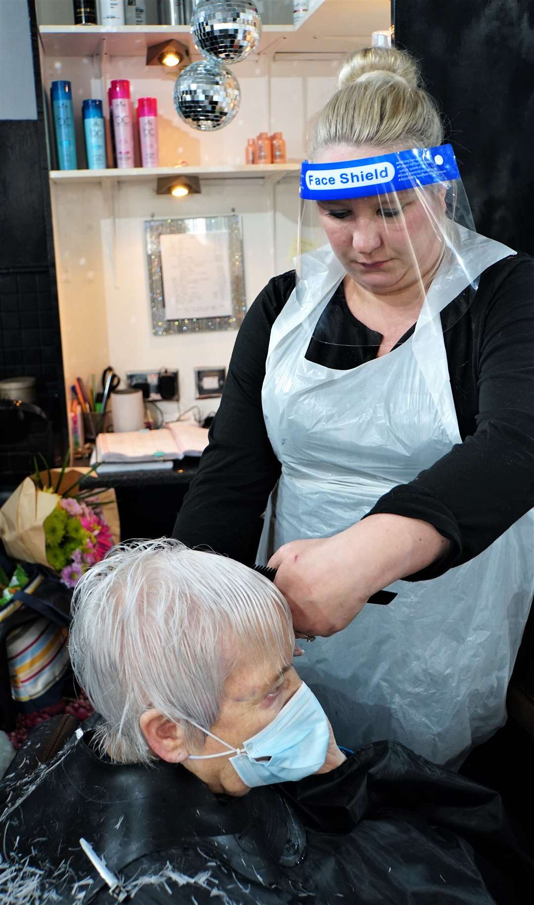 Amanda Bruce wears a protective visor as she snips away on Ella Henderson's hair.
