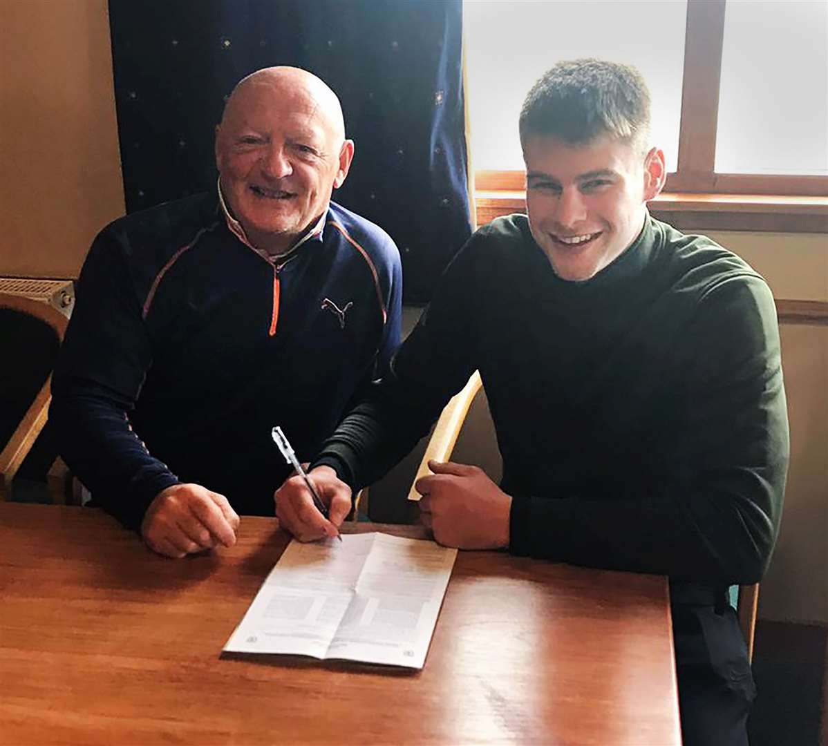 Wick Academy striker Marc Macgregor signing his new deal as club chairman Pat Miller looks on.
