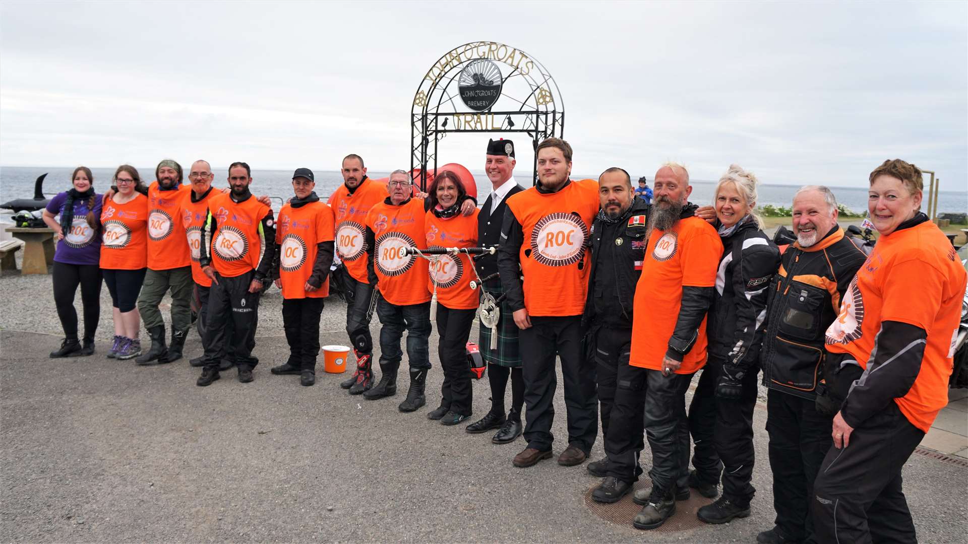 The Riders of Charity line up with Wick piper Colin Mackay at the new John O'Groats archway. Pictures: DGS