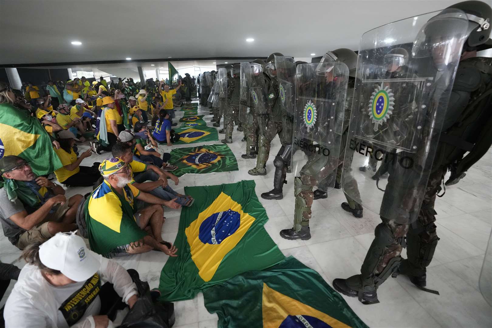 Protesters supporting Brazil’s former president Jair Bolsonar sit in front of police after inside Planalto Palace after storming it (Eraldo Peres/AP)