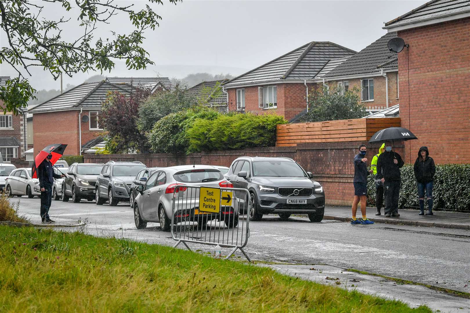 A long queue of cars is directed by a marshall before accessing the walk-in coronavirus testing centre at Caerphilly Leisure Centre (Ben Birchall/PA)