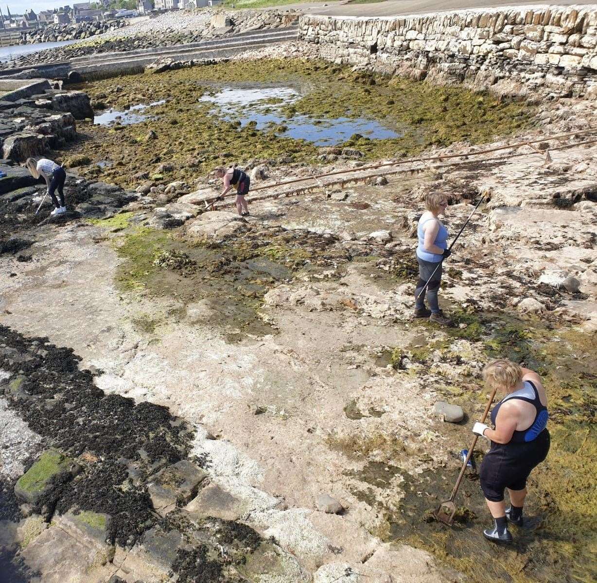 Patty Coghill (front) along with some of the other volunteers who helped to scrape out all the seaweed and pressure wash around the sides of the North Baths on Saturday.