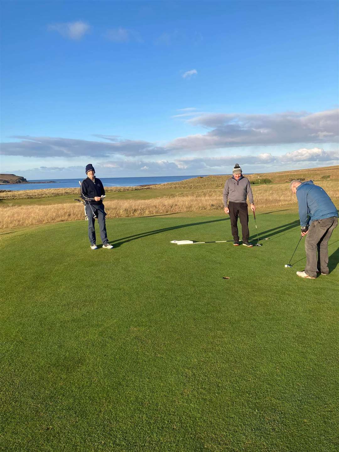 Bruce Mackay putting at the first hole while Donald Mowat and Cammie Ross