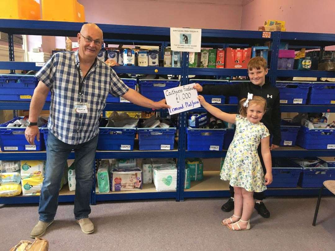 Caithness Foodbank chairman Grant Ramsay accepting the 'cheque' from Jayden and Layla Bremner at a two-metre distance.