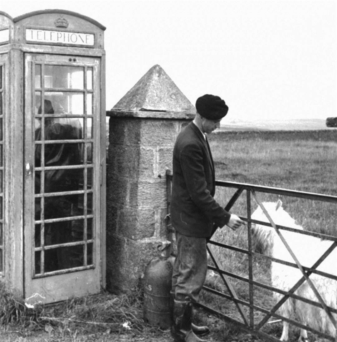 Jimmy Aitken, one of the Stroma lighthouse keepers, feeding a goat at a gate alongside the island's phone box, close to the church.