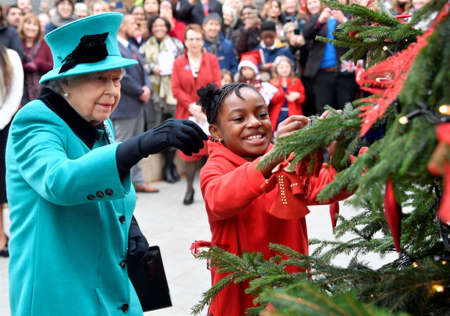 Queen Elizabeth II and Shylah Gordon-Clarke, then 8, attach a bauble to a Christmas tree during her visit to Coram, the UK’s oldest children’s charity (PA)