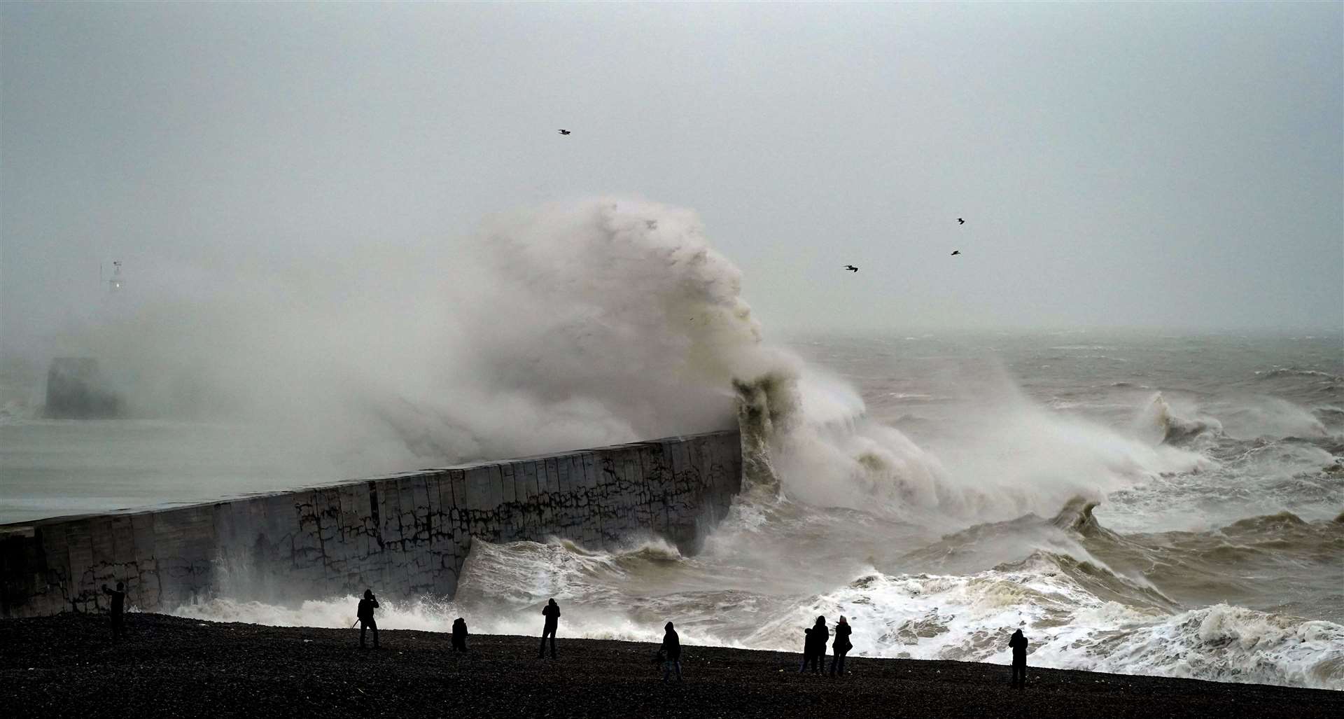 Onlookers are dwarfed by huge waves crashing over Newhaven lighthouse at West Quay in East Sussex (Steve Parsons/PA)