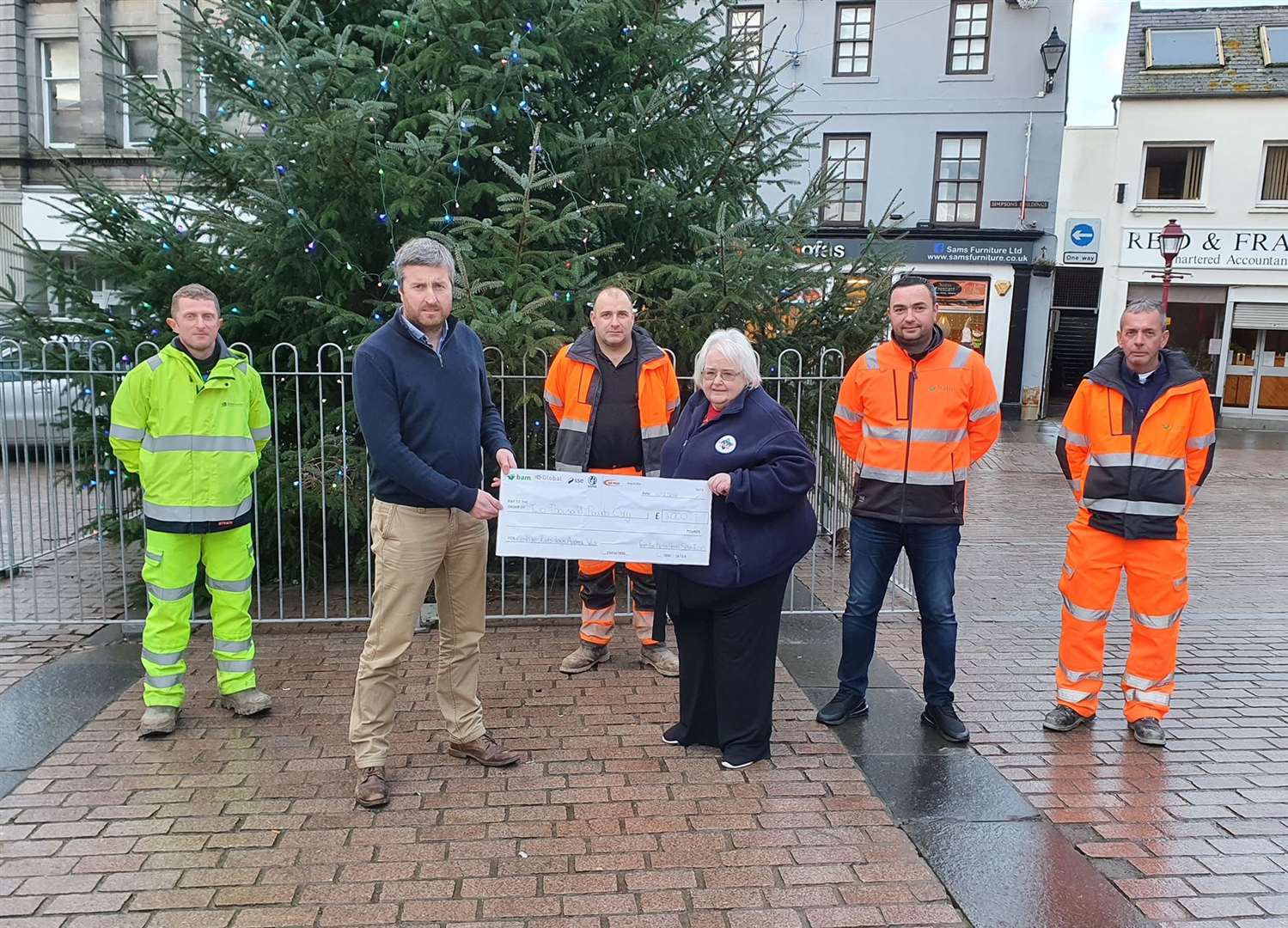 Jackie Johnson of Caithness FM accepting the cheque from representatives of BAM Nuttall and SSEN Transmission in front of Wick's Christmas tree.