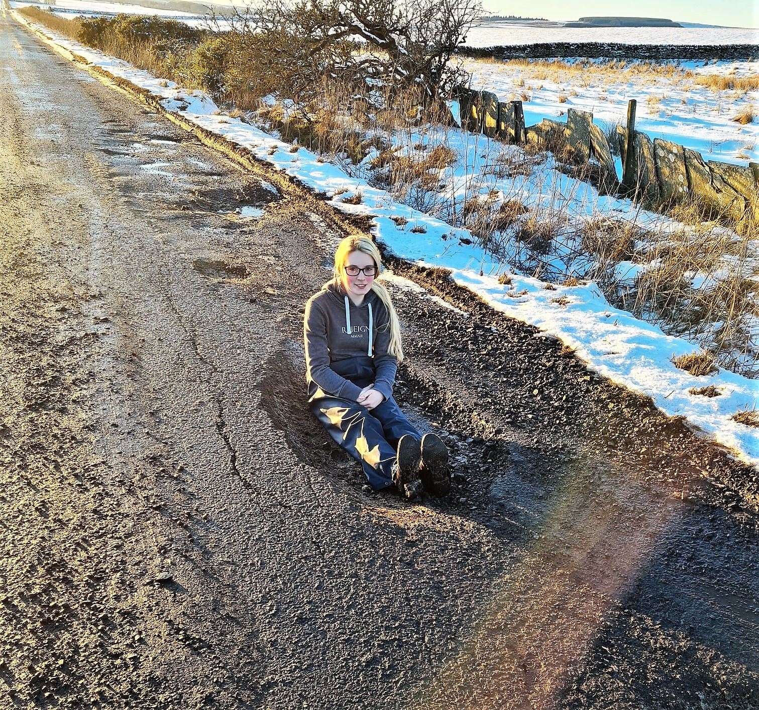 Megan Gillon from Lieurary sitting in a pothole that wrecked two wheels of her car – she quipped that the pothole was so big she could have had a bath in it. Picture: Kirsty Gillon