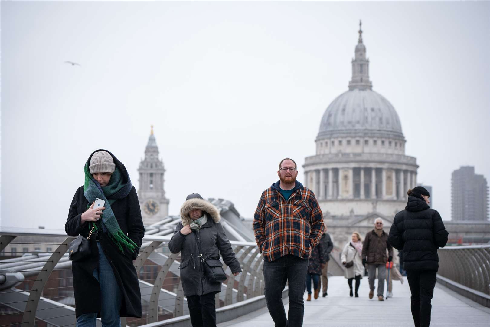 Pedestrians shield themselves from the wind and rain as they cross the Millennium Bridge, in London (Dominic Lipinski/PA)