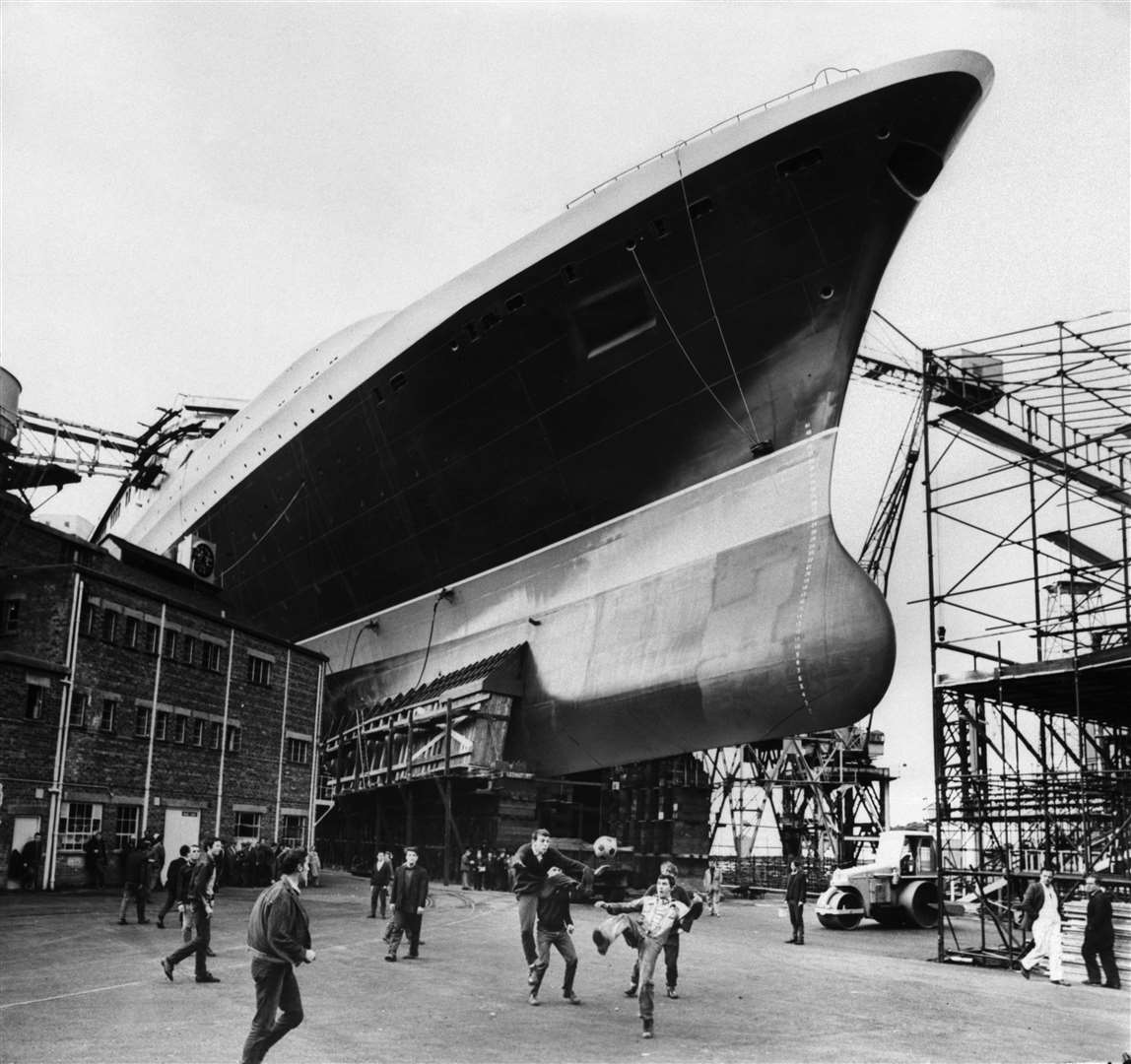 A group of young men play football beneath the hull of the QE2 in a shipyard in Clydebank, Scotland, in 1967 ( Mirrorpix/PA)