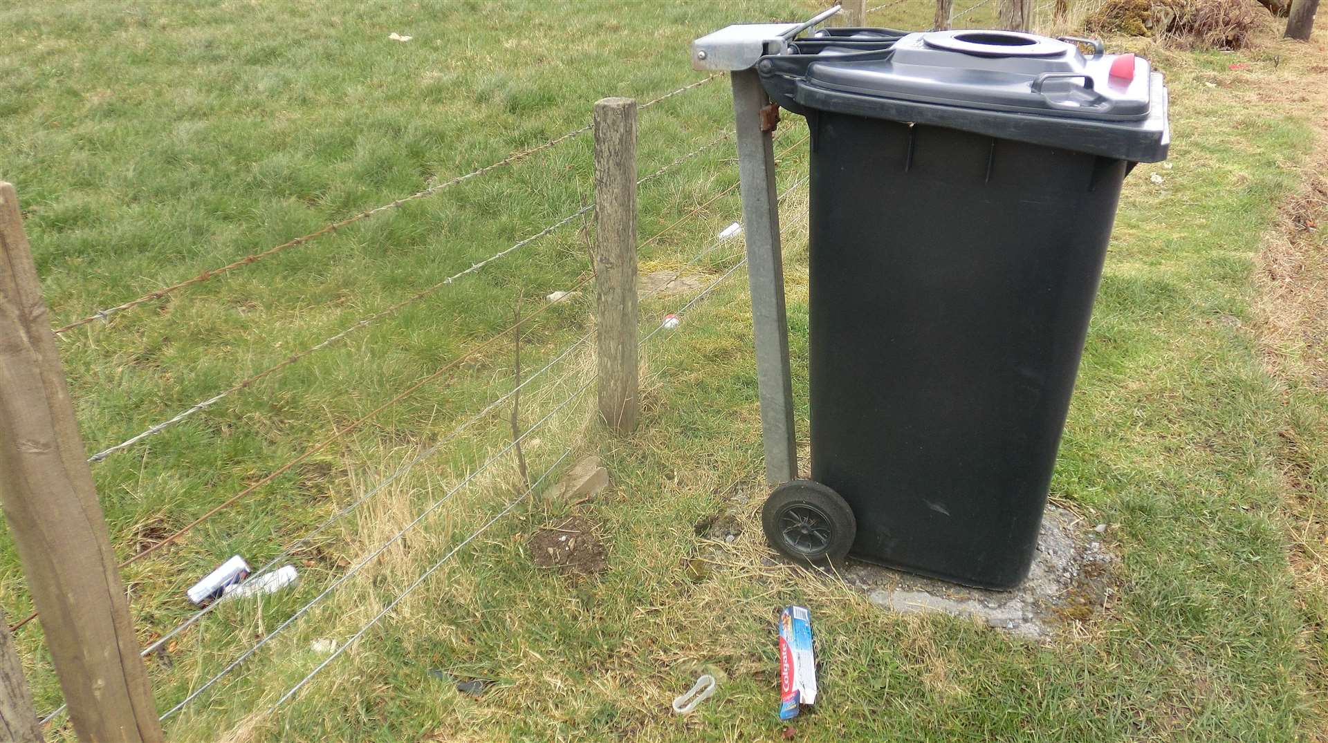 A Highland Council bin lies along the lay-by and rubbish lies next to it.