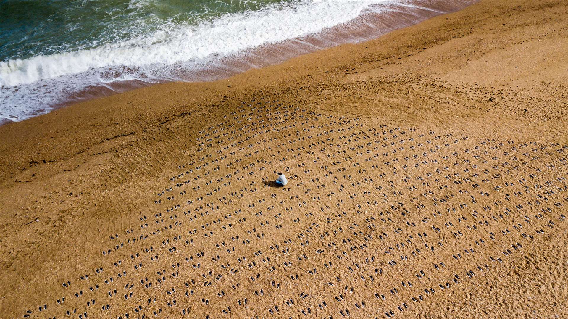 Artist Martin Barraud works on an installation of 749 pairs of bootprints at Slapton Sands in Devon where 749 American soldiers were killed while rehearsing for the D-Day invasion of Normandy (There But Not There/PA)