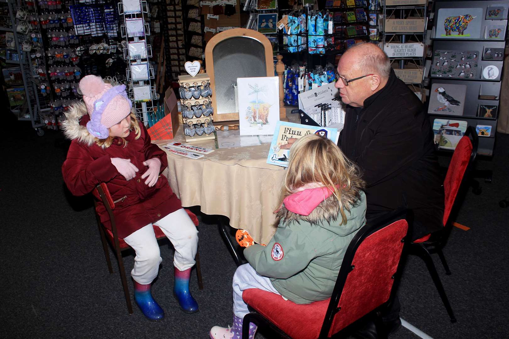 Ian Leith reading the John O'Groats children's book Finn and Friends to young visitors Olivia (8) and Frankie (5) at the Groatie Buckie Gift Shop.