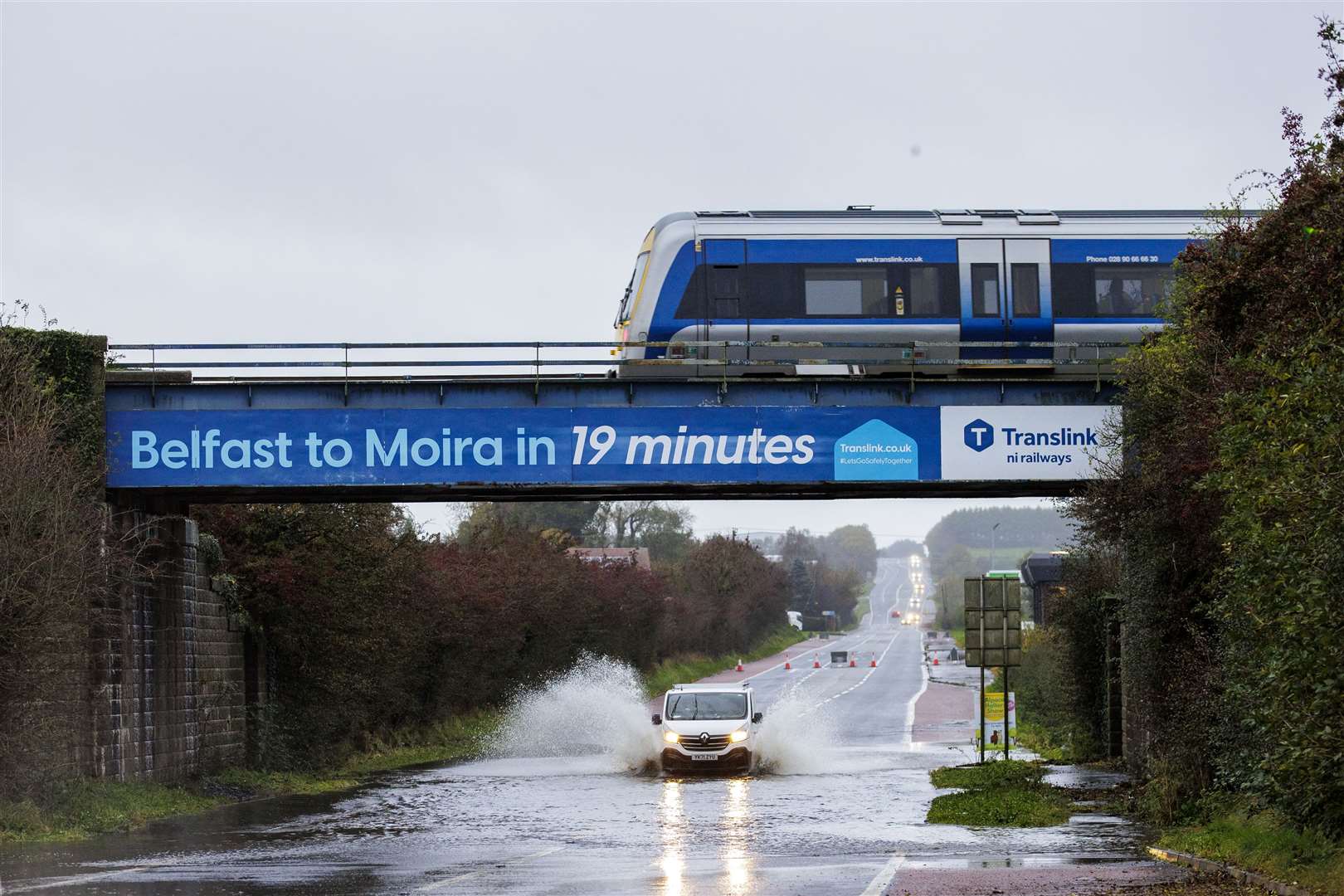 A van drives through a flooded area under a railway bridge as a train passes overhead on the A26 outside the village of Moira in Northern Ireland (Liam McBurney/PA).