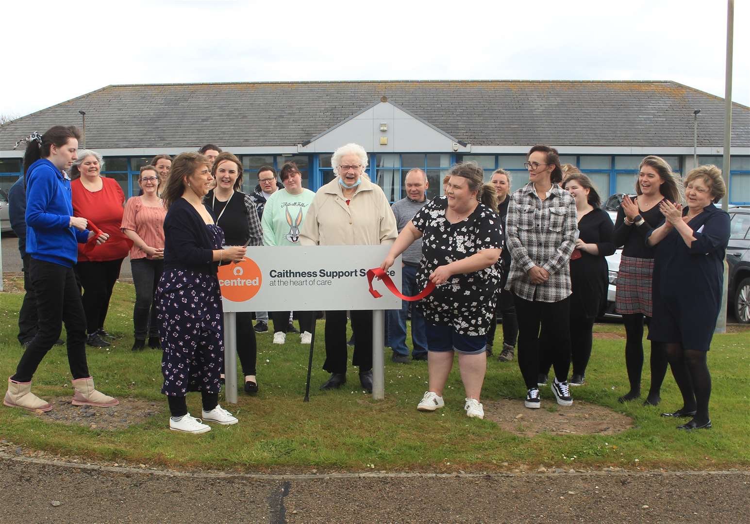 Amiee Marks (front, left) cutting the ribbon along with Kelsie O'Brien (front, right) and Stacy McIntosh (left), watched by staff and guests outside the Centred base in Wick on Friday.