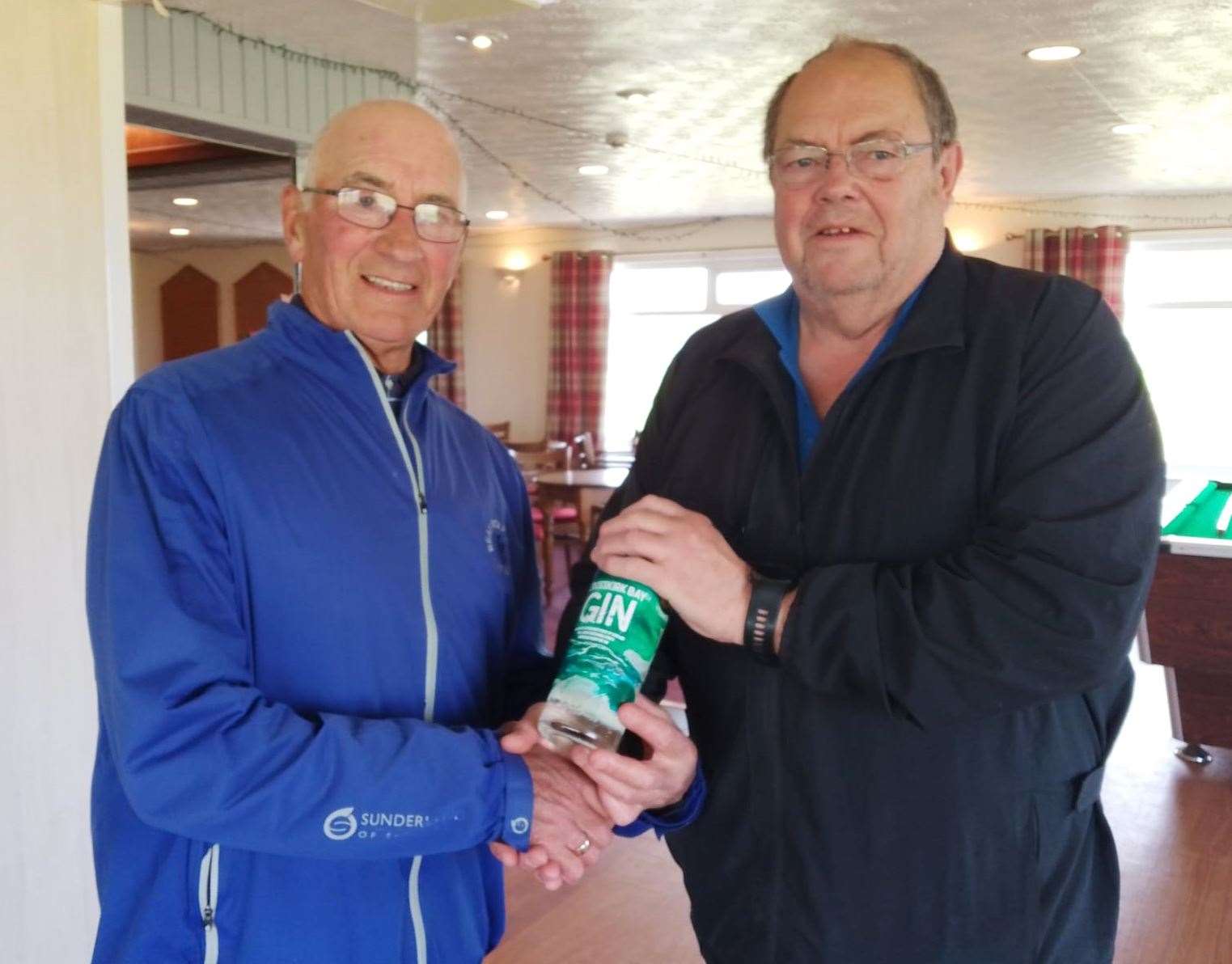 Alistair Gunn (left) receiving the nearest-the-pin prize, a bottle from North Point Distillery, from Mike Halliday after winning it in the Senior Stableford competition.