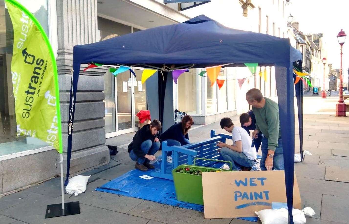 Volunteers from local groups paint up a bench to brighten the High Street.