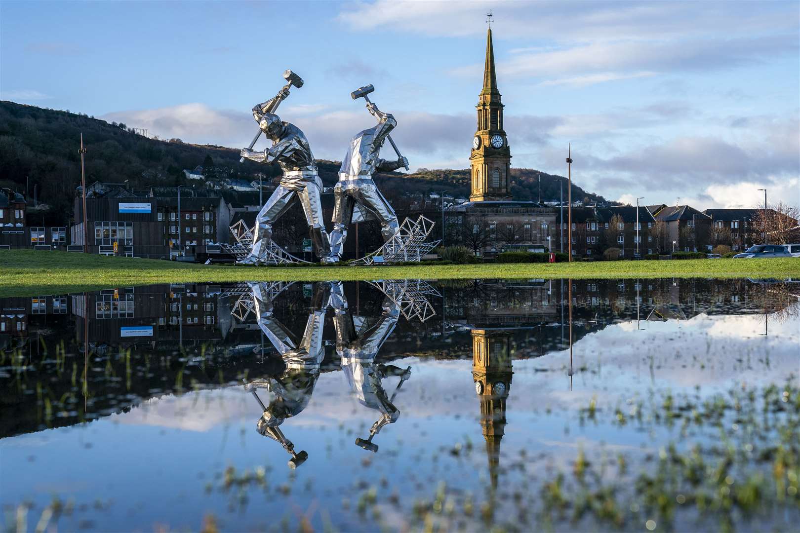 The Shipbuilders of Port Glasgow sculpture in Coronation Park, Inverclyde, is reflected in large puddles after heavy downpours (Jane Barlow/PA)