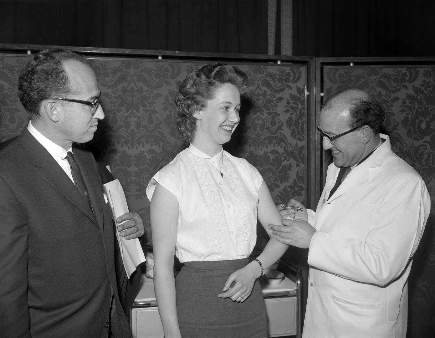 Dr Jonas Salk, left, the American polio vaccine pioneer, watches as 21 year old Margaret Jenkins becomes the 500,000th person to complete the two injection anti-polio course in London (PA)