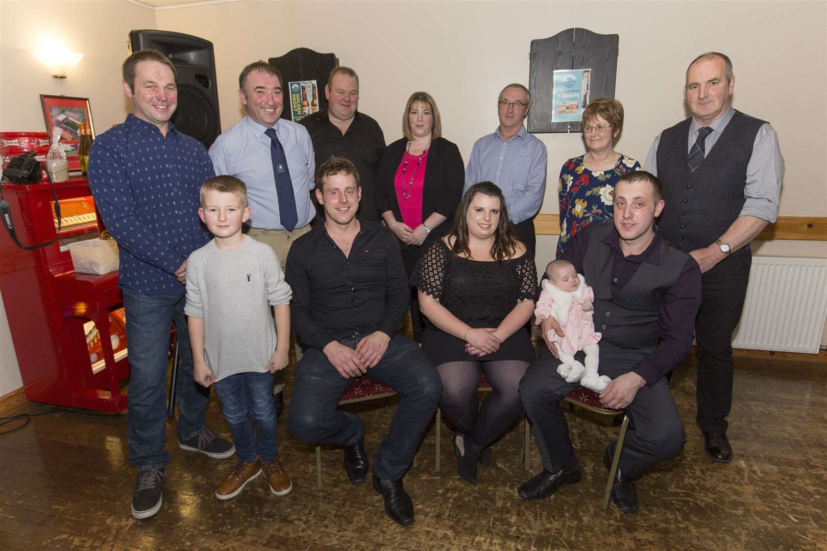 Canisbay Show chairman Stuart Sinclair (seated, left), secretary Leeann Hope (seated, centre) and vice-chairman Jamie Coghill, who was literally left holding the baby, 12-week-old Iona Mackay, while her parents joined some of the other show helpers in the back row. Picture: Robert MacDonald / Northern Studios