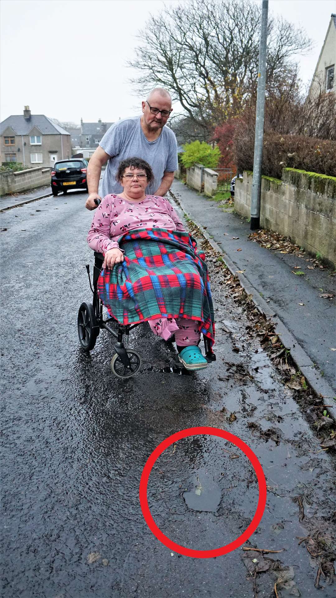 Janet with her partner Ronnie on West Banks Terrace beside the deceptively deep pothole which caused the accident in October last year. Picture: DGS