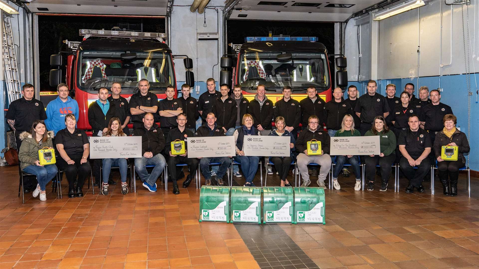 Some of the Thurso firefighters with the defibrillators the security cabinets, and representatives of the local premises where the lifesaving devices will be installed, as well as members of the four community receiving cheques. Picture: Stevie Bruce