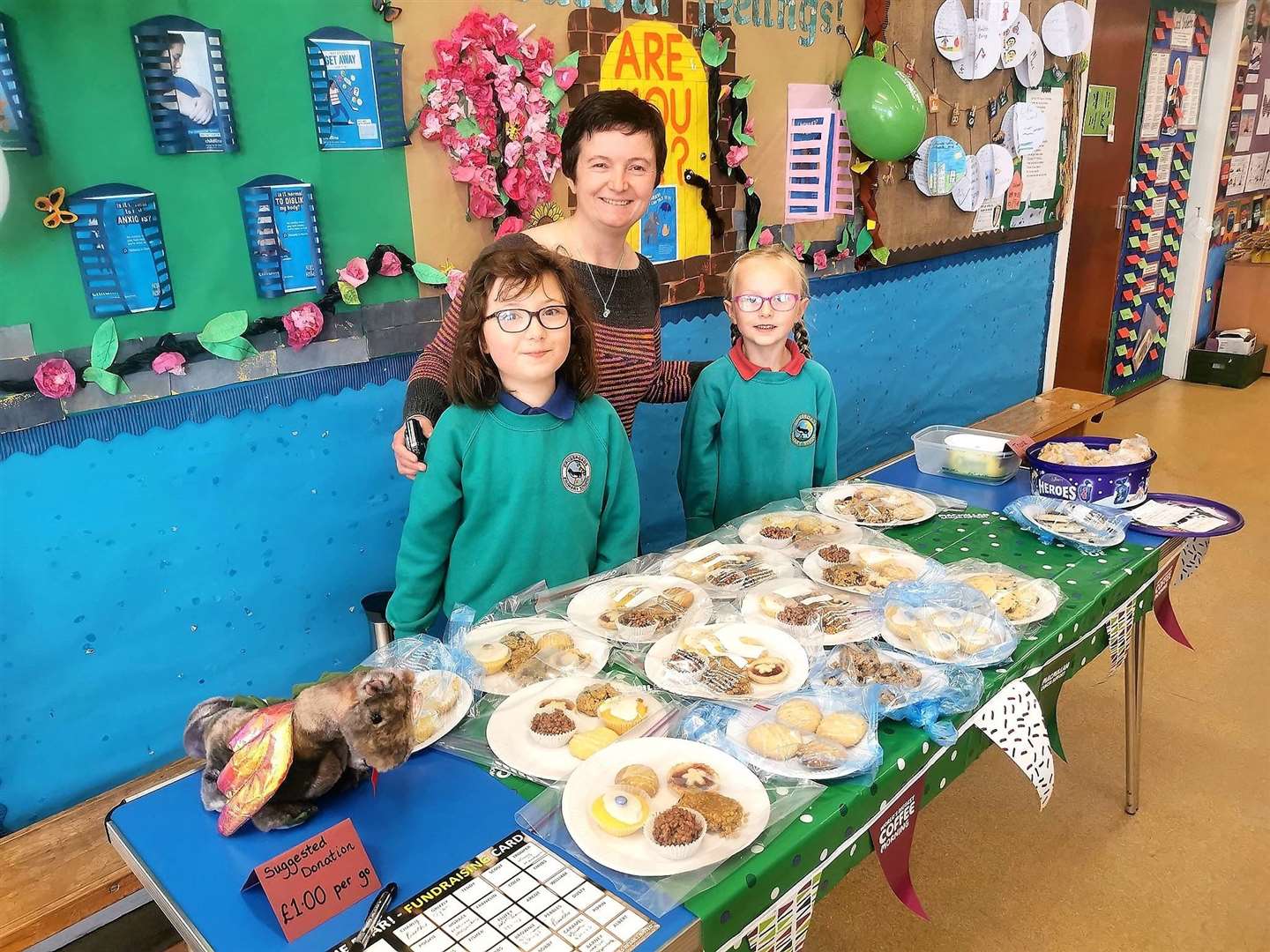 Louise Hunt, clerical assistant, and pupils Skye Macdonald and Ellie Fogarty-Macdonald with the bake sale and Dusty the dragon.