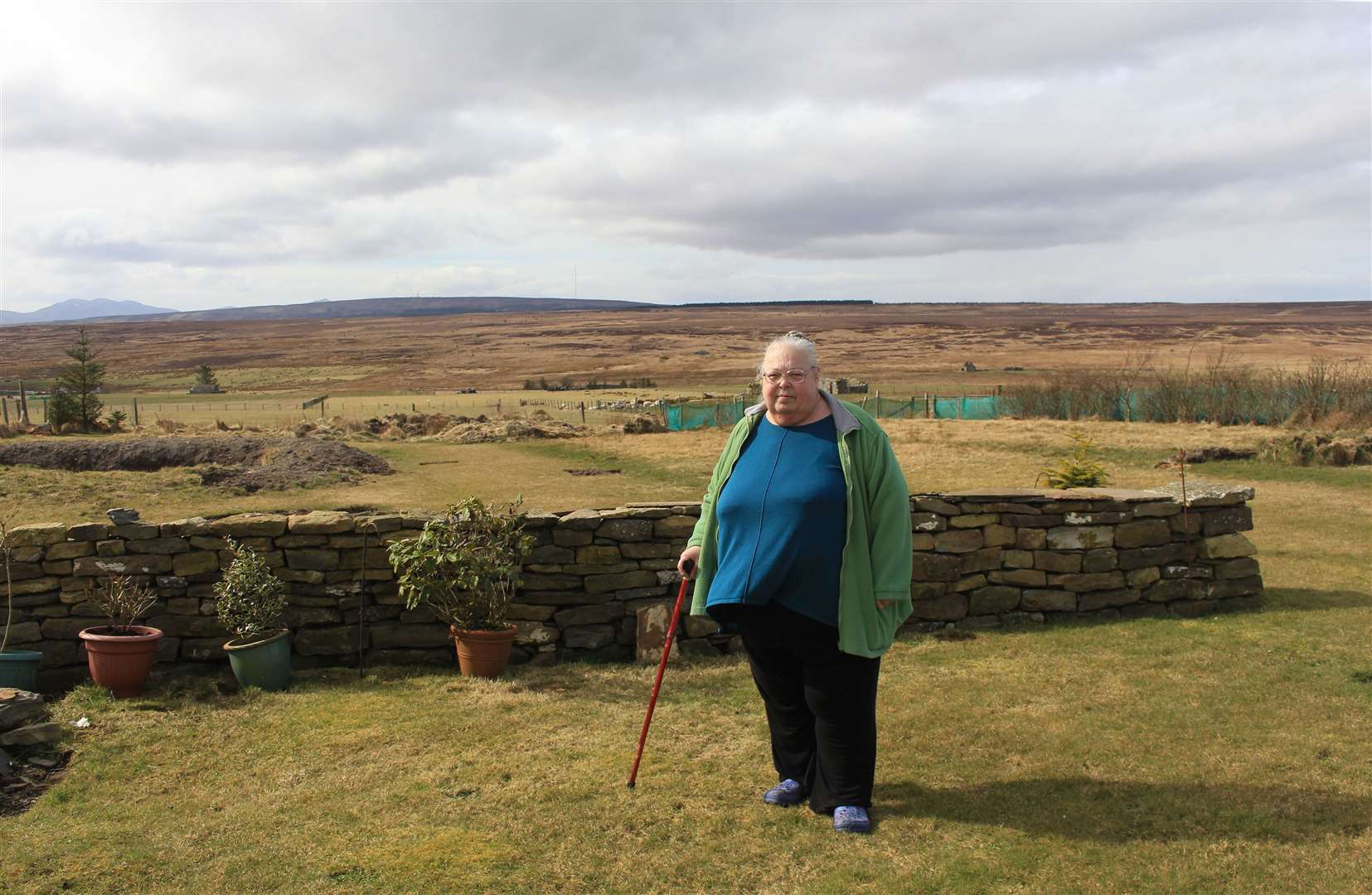 Jo Bowd outside her cottage at Roster, north of Lybster, with the Golticlay Wind Farm development site in the distance. Picture: Alan Hendry