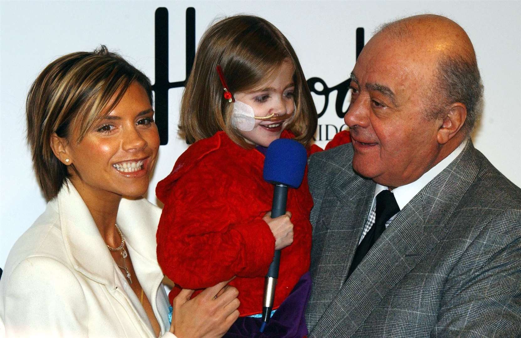Victoria Beckham and Mohammed Al Fayed help with six-year-old Kirsty Howard from Manchester, who was born with her heart back to front, open the Harrods’ January sales in 2002 (PA)