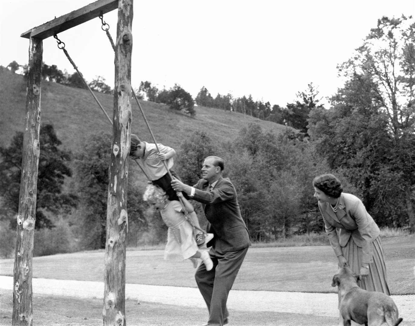 Prince Charles and Princess Anne being pushed on a swing by their father, the Duke of Edinburgh, with their mother looking on at Balmoral (PA)