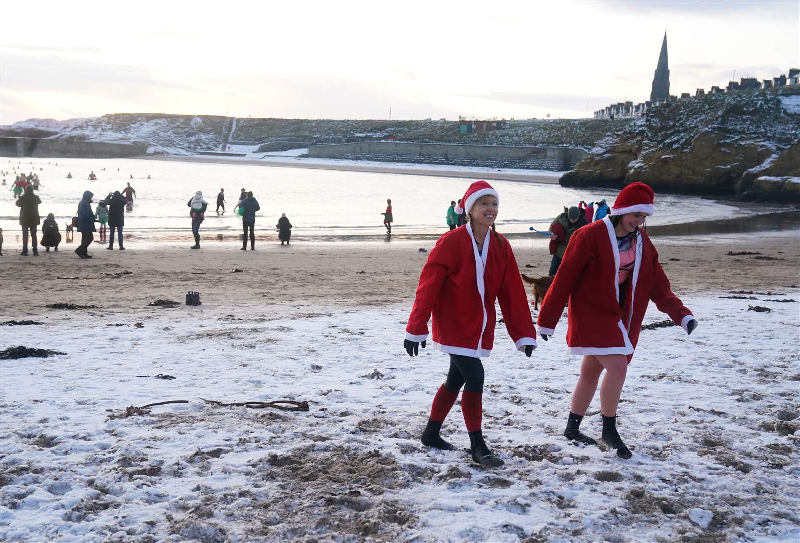Cold water swimmers walk on a snow-covered beach at Cullercoats Bay on the North East coast (Owen Humphreys/PA)