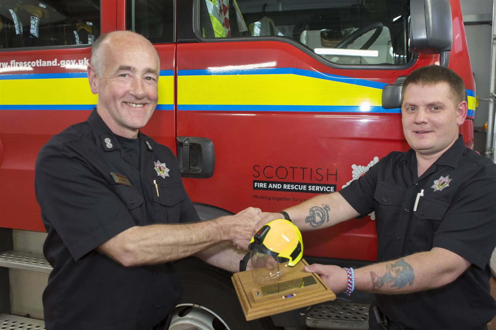Robert Gunn receives a mounted replica of a fire fighters helmet from Wick Watch Commander Hugo Ross (left). Picture: Robert MacDonald/Northern Studios