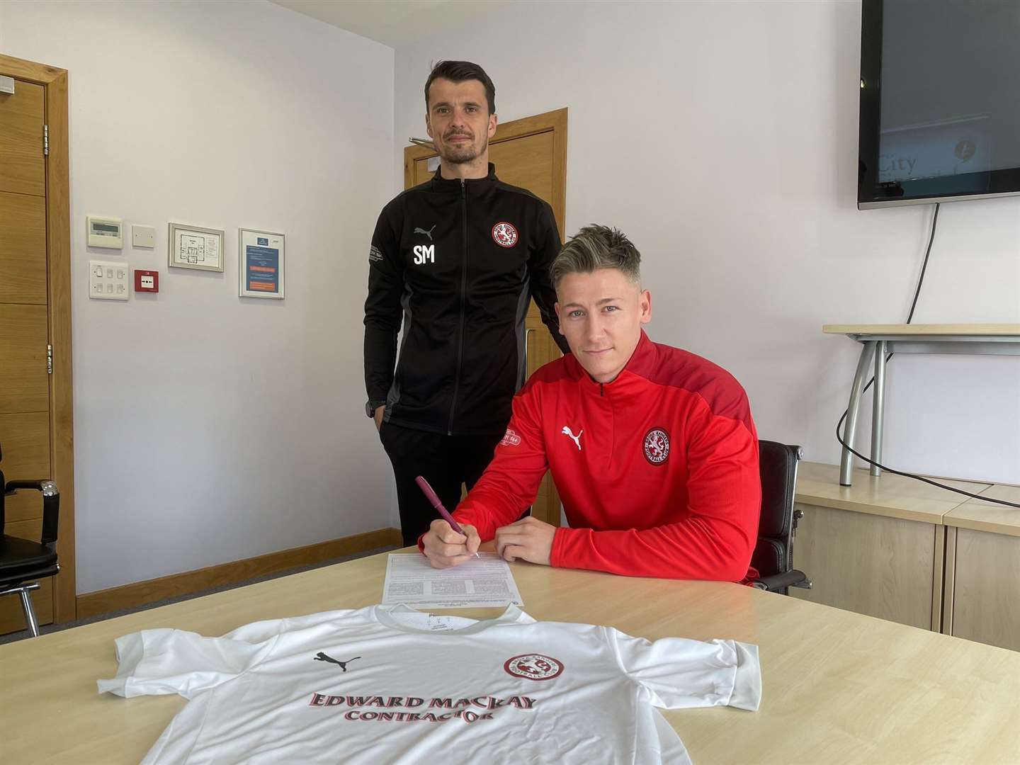 Josh Meekings signing for Brora Rangers as manager Steven Mackay looks on.