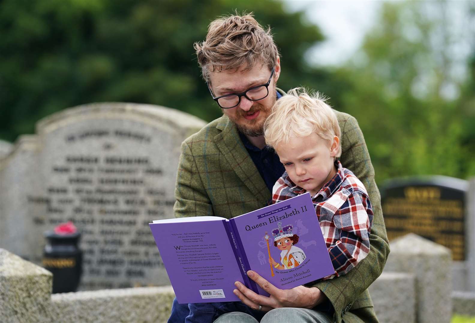 Robert Henning reads a story for his son Arthur, three, at the picnic at St Bartholomew’s Parish Church, Newry (Brian Lawless/PA)